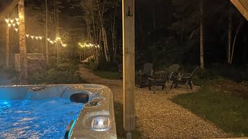 Un jacuzzi con un sendero que lleva a una zona de estar al aire libre, rodeado de árboles y luces colgantes.