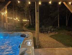 A hot tub with a pathway leading to outdoor seating, surrounded by trees and string lights. - Grand Aylmer, SPA, Bord De l'eau (Beaulac-Garthby)