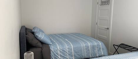 Un dormitorio pequeño y ordenado con cama, mesita de noche y puerta.