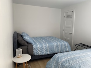 Quarto pequeno e bem arrumado, com uma cama, mesa de cabeceira e uma porta.