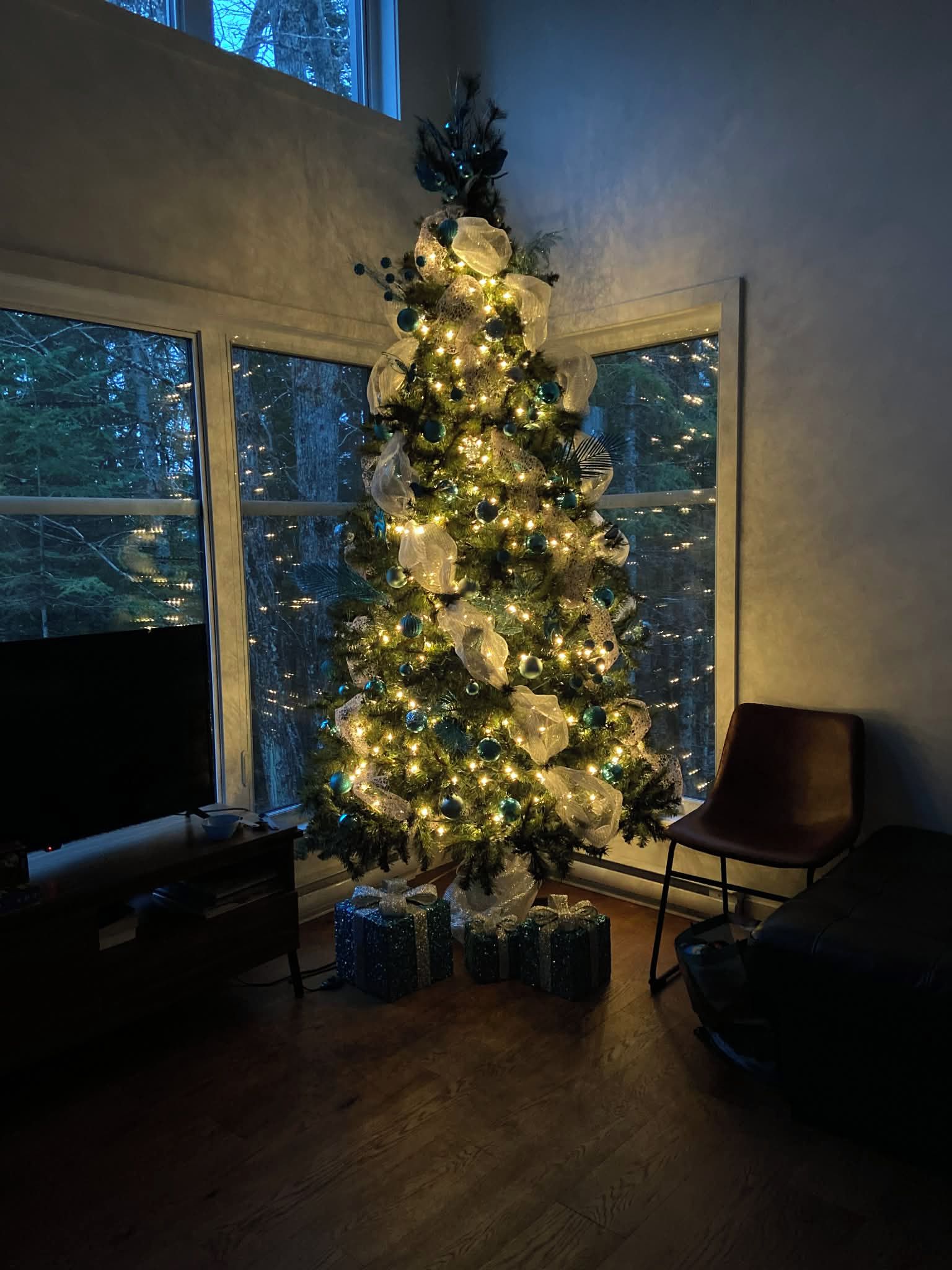 Un árbol de Navidad con luces y adornos en una habitación con un ventanal grande.