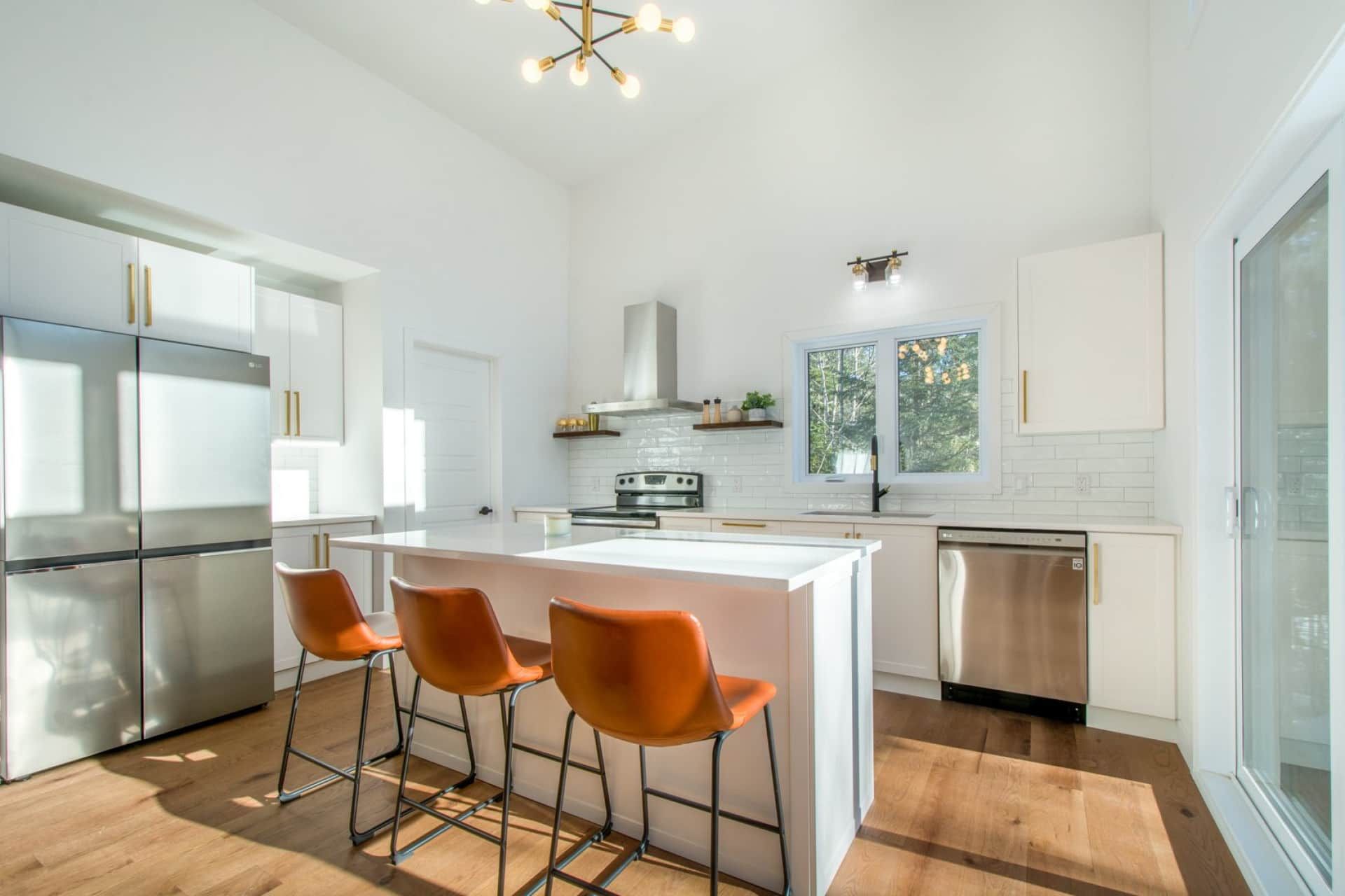 A modern kitchen with a central island, stainless steel appliances, and a large window.