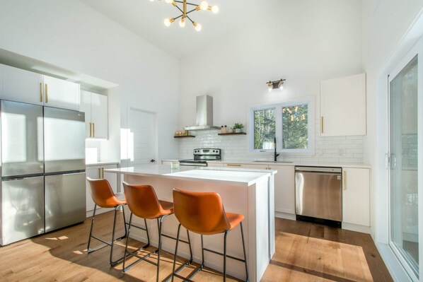 A modern kitchen with a central island, stainless steel appliances, and a large window. - Grand Aylmer, SPA, Bord De l'eau (Beaulac-Garthby)