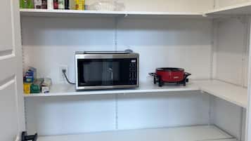 Una cocina con estantes blancos, un microondas, una olla de cocción lenta roja y una tetera.