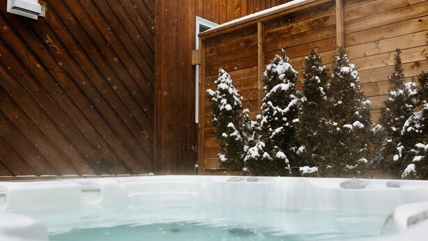Uma banheira de hidromassagem com um deck de madeira e árvores cobertas de neve ao fundo.