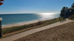 A coastal view with a clear sky, a beach, and a building with a balcony overlooking the sea. - Upper River House Waterfront Getaway on Ahnapee River with Dock Boat Slip Wifi (Algoma)