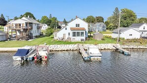 A waterfront property with a dock, a house with a large window, and a grassy yard. - Upper River House Waterfront Getaway on Ahnapee River with Dock Boat Slip Wifi (Algoma)