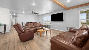 A spacious living room with leather sofas, a wooden coffee table, and a ceiling fan.