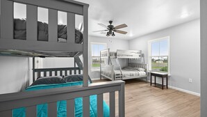 A room with bunk beds, a ceiling fan, and large windows.