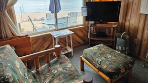 A cozy room with a wooden interior, a television, a table with chairs, and a view of the beach.