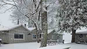 A snow-covered picnic table in a park with wooden cabins in the background.