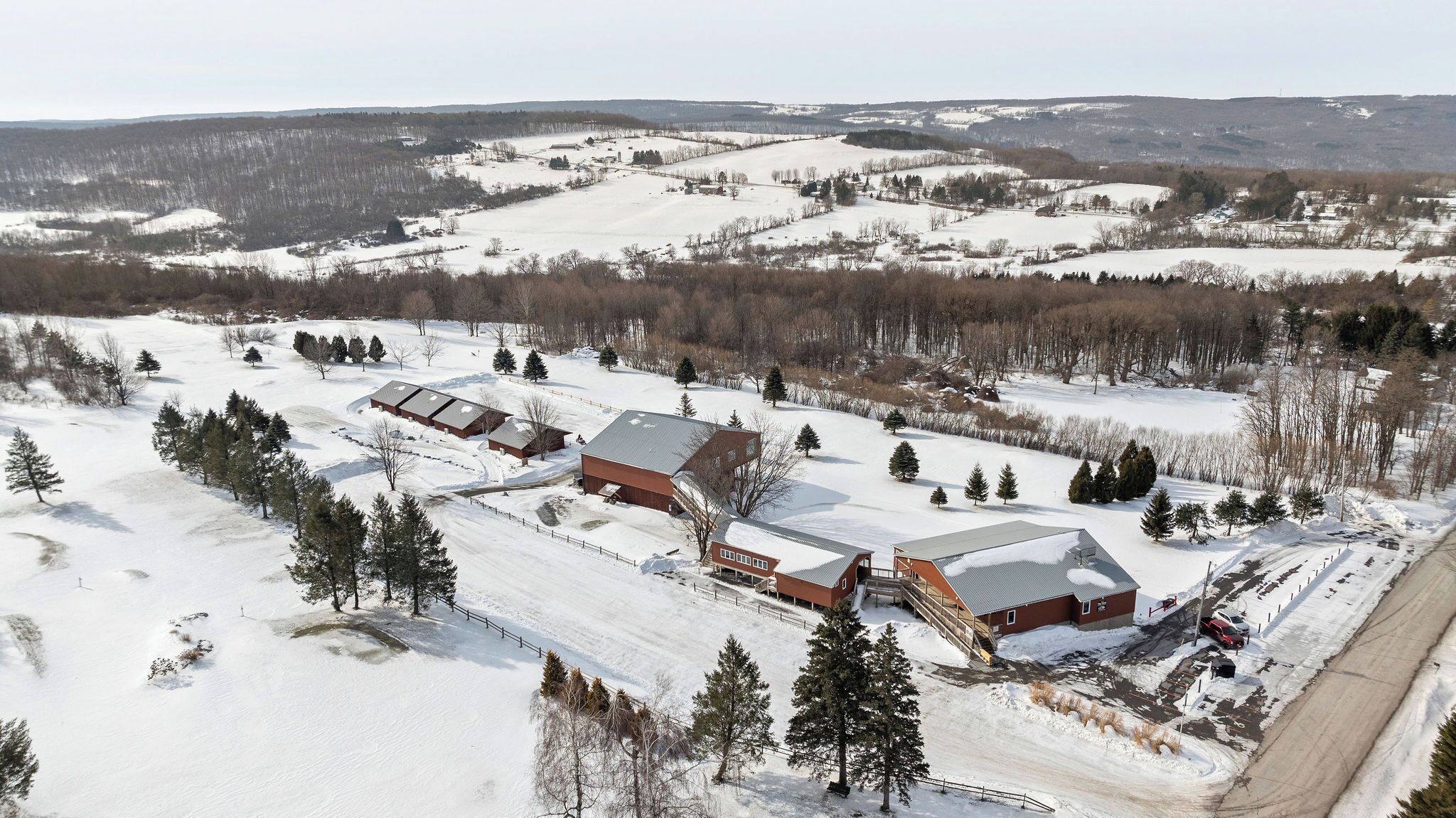 Une vaste propriété enneigée comprenant plusieurs bâtiments, dont une maison principale et plusieurs granges, le tout entouré d’arbres et de champs ouverts.