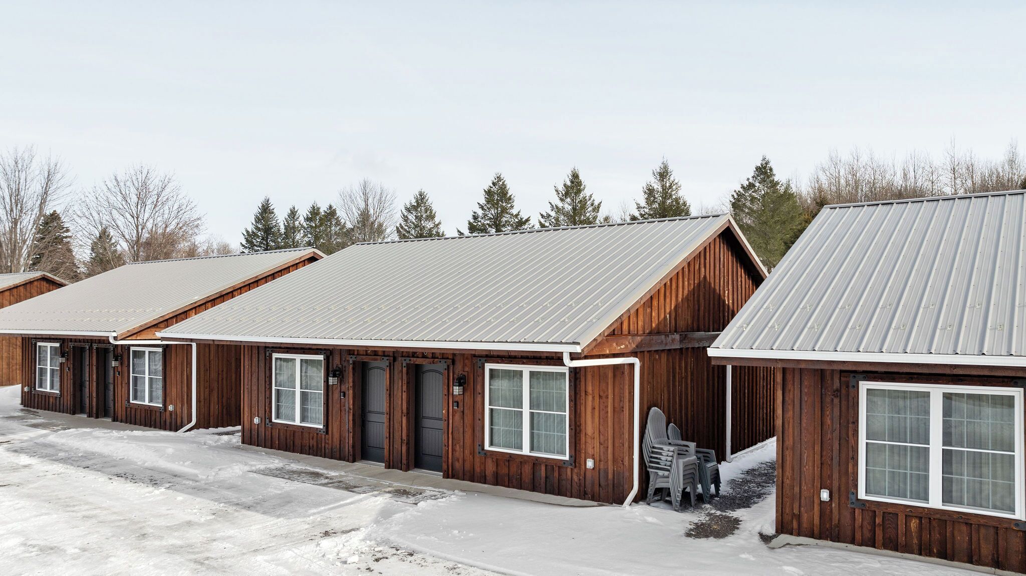 Une rangée de cabanes en bois, coiffées de toits en métal, chacune dotée d’une porte d’entrée et de fenêtres.