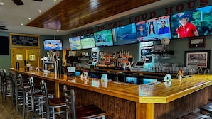 A bar area with multiple screens displaying sports events, a wooden bar counter, and several bar stools. - Golf, Outdoor Bar, Restaurant - The Timber Cabin (Tully)