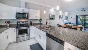 A modern kitchen with white cabinets, stainless steel appliances, granite countertops, and a dining area with a table and chairs.