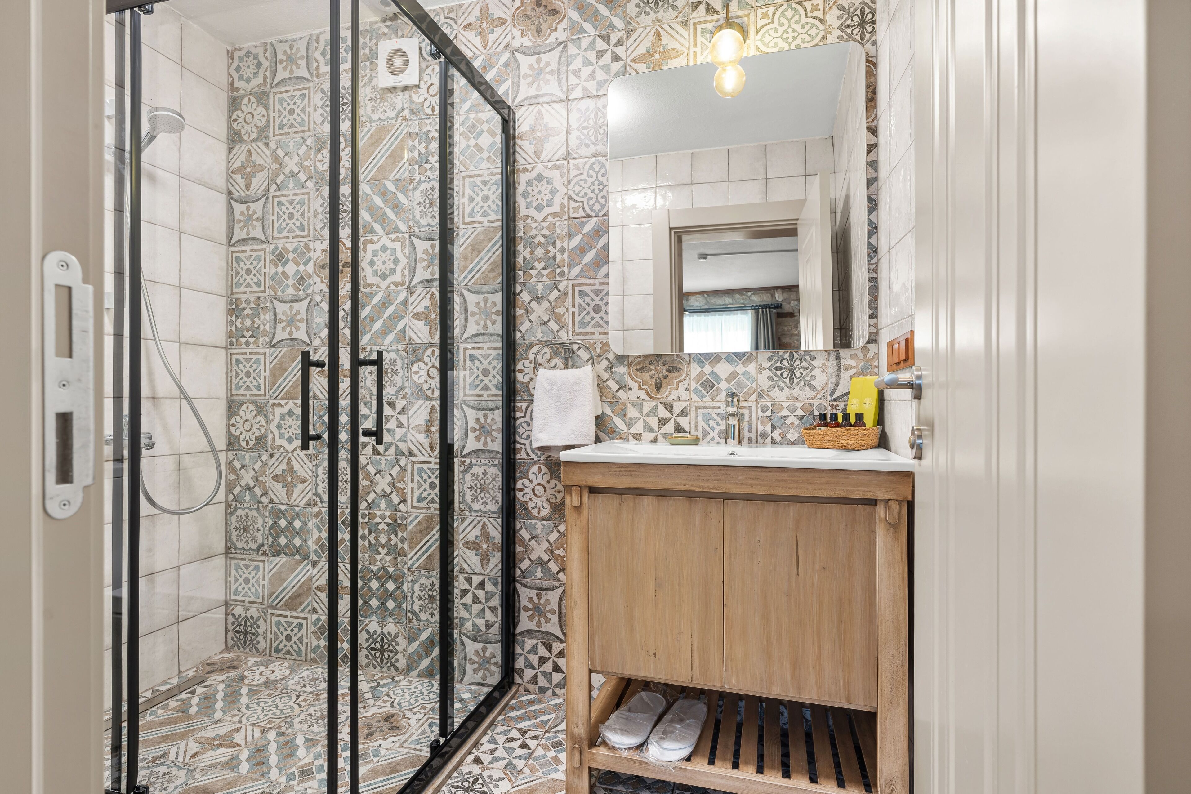 A bathroom with a shower, tiled walls, a wooden vanity, and a mirror.