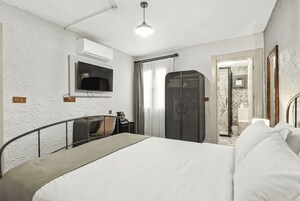 Un dormitorio con cama, televisión montada en la pared, armario y baño visible a través de una puerta abierta.