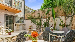 Un patio al aire libre con mesas y sillas redondas, un jarrón con flores y un edificio con balcón.