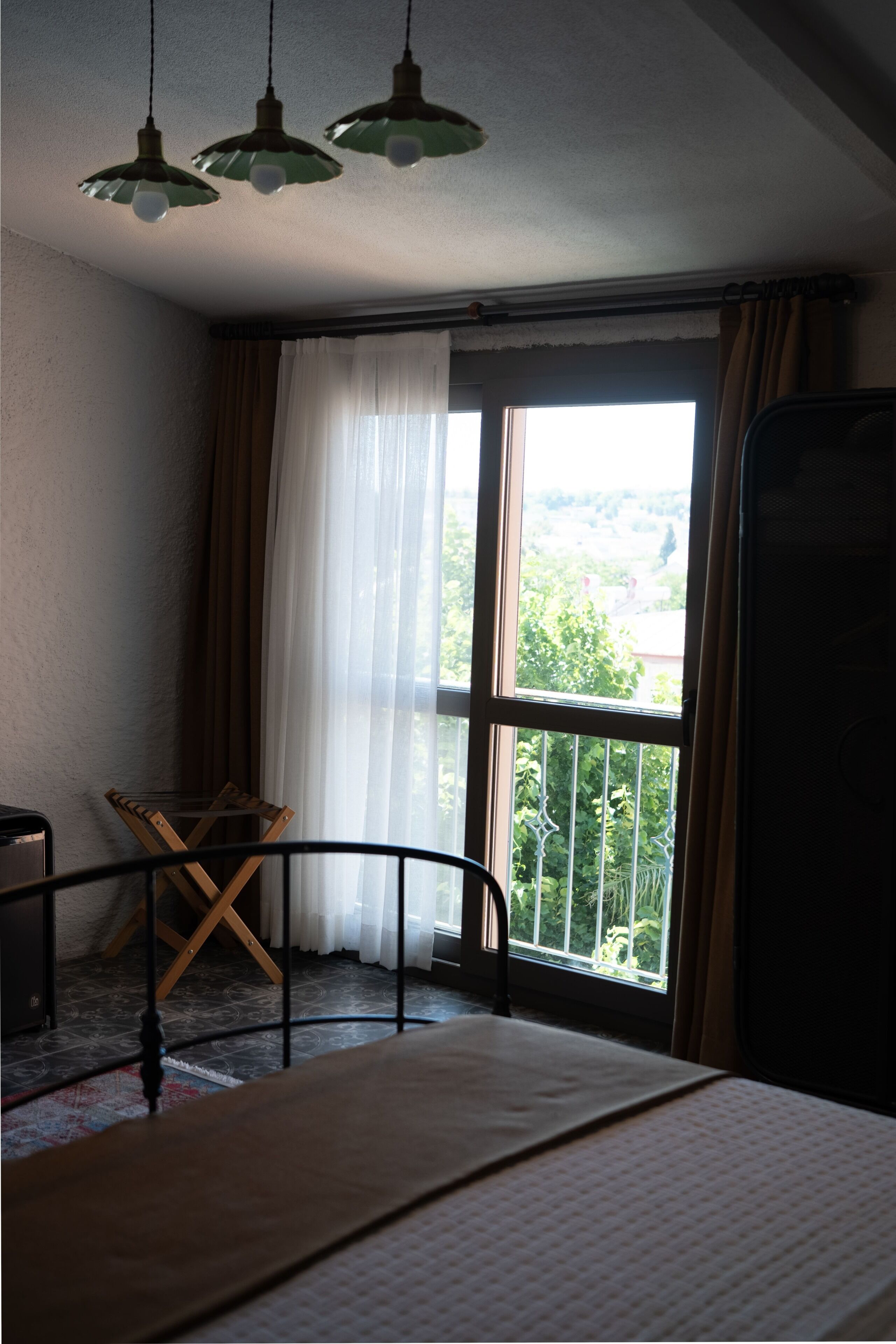 Una stanza con un letto, una sedia, una finestra con tende e un balcone.