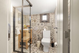 Un baño con cabina de ducha de vidrio, inodoro, lavamanos con espejo y azulejos estampados.