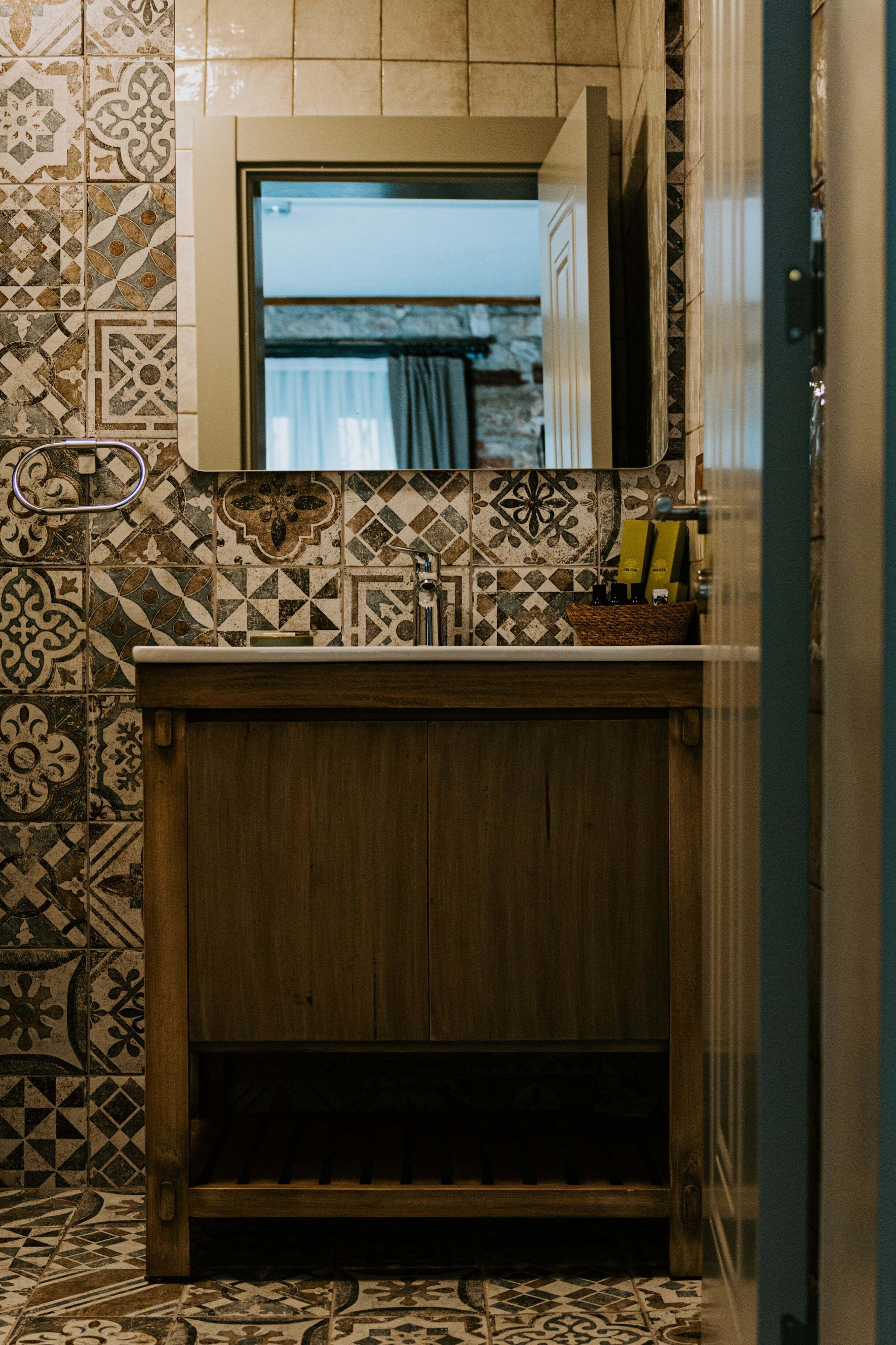 Un baño con tocador de madera, azulejos estampados y un espejo sobre el lavabo.