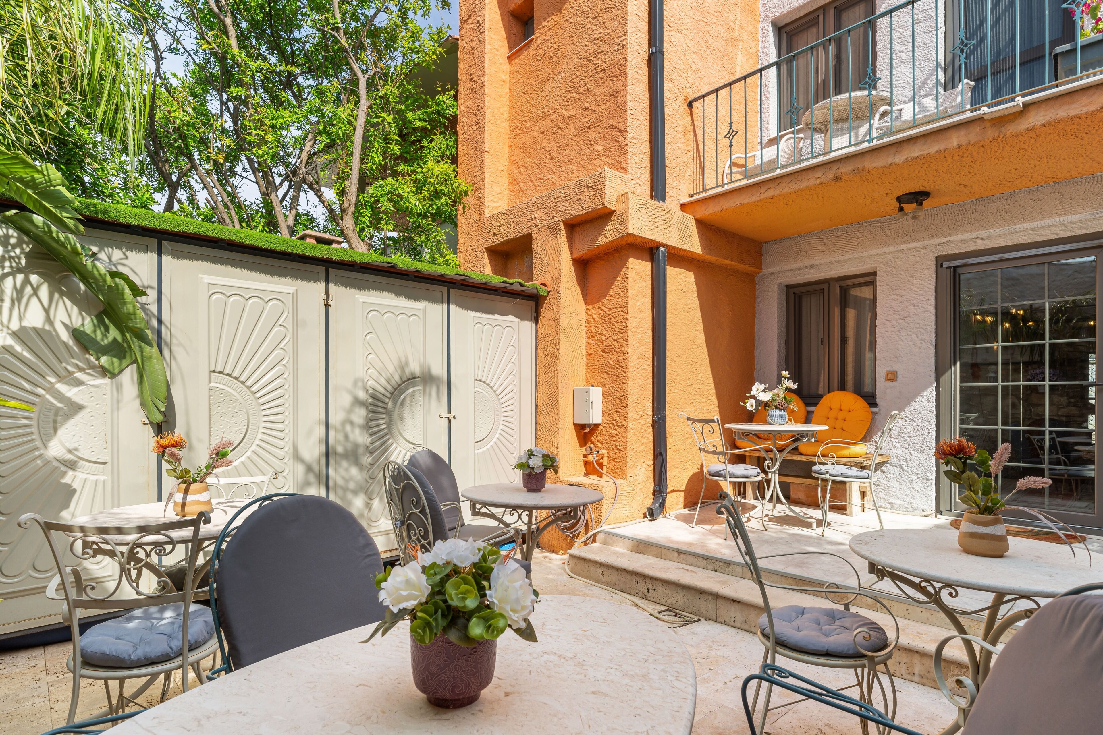 An outdoor patio with tables and chairs, a decorative wall, and a balcony with a railing.