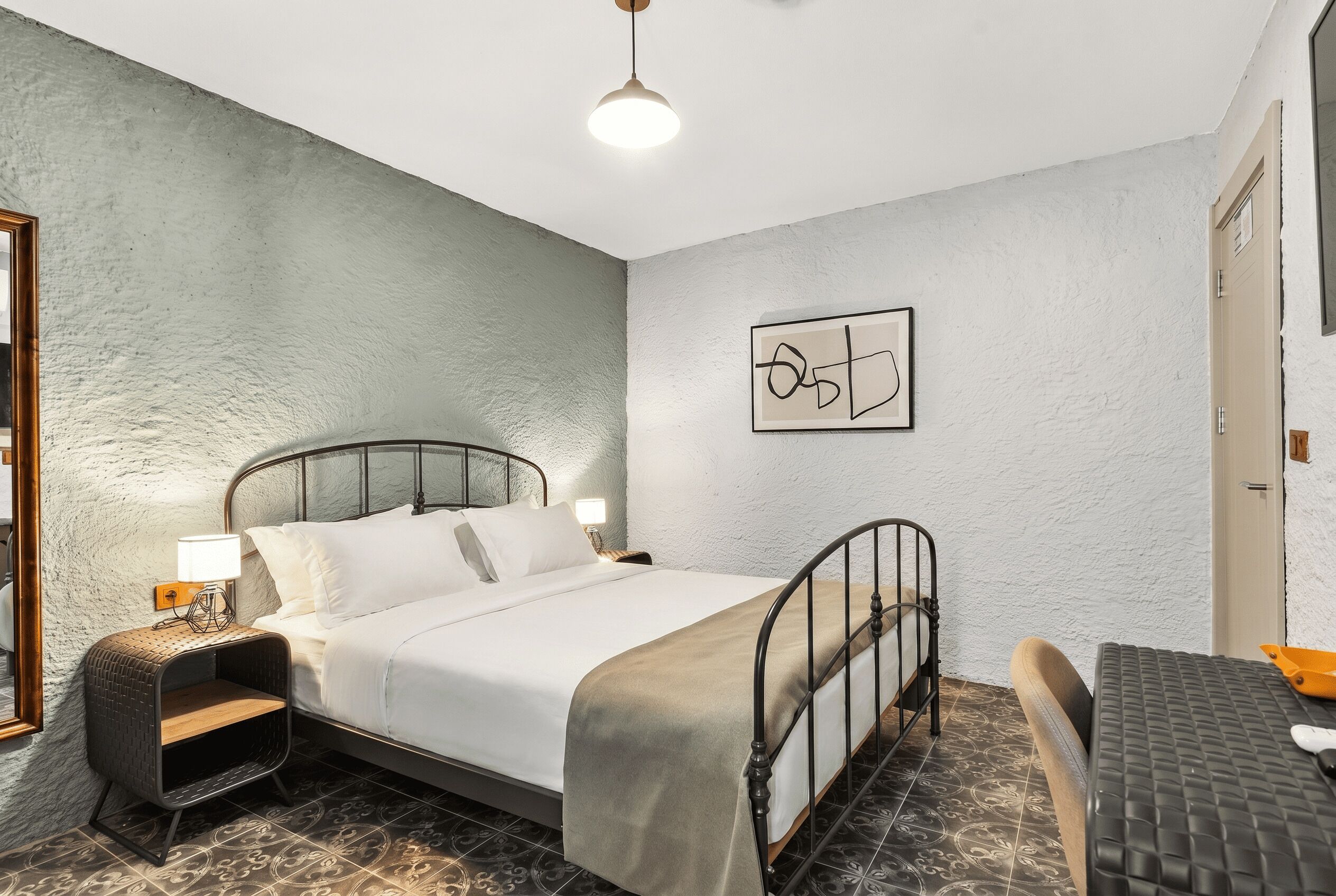 Una cama individual con cabecera, una mesita de noche con lámpara, una silla y un cuadro en la pared.