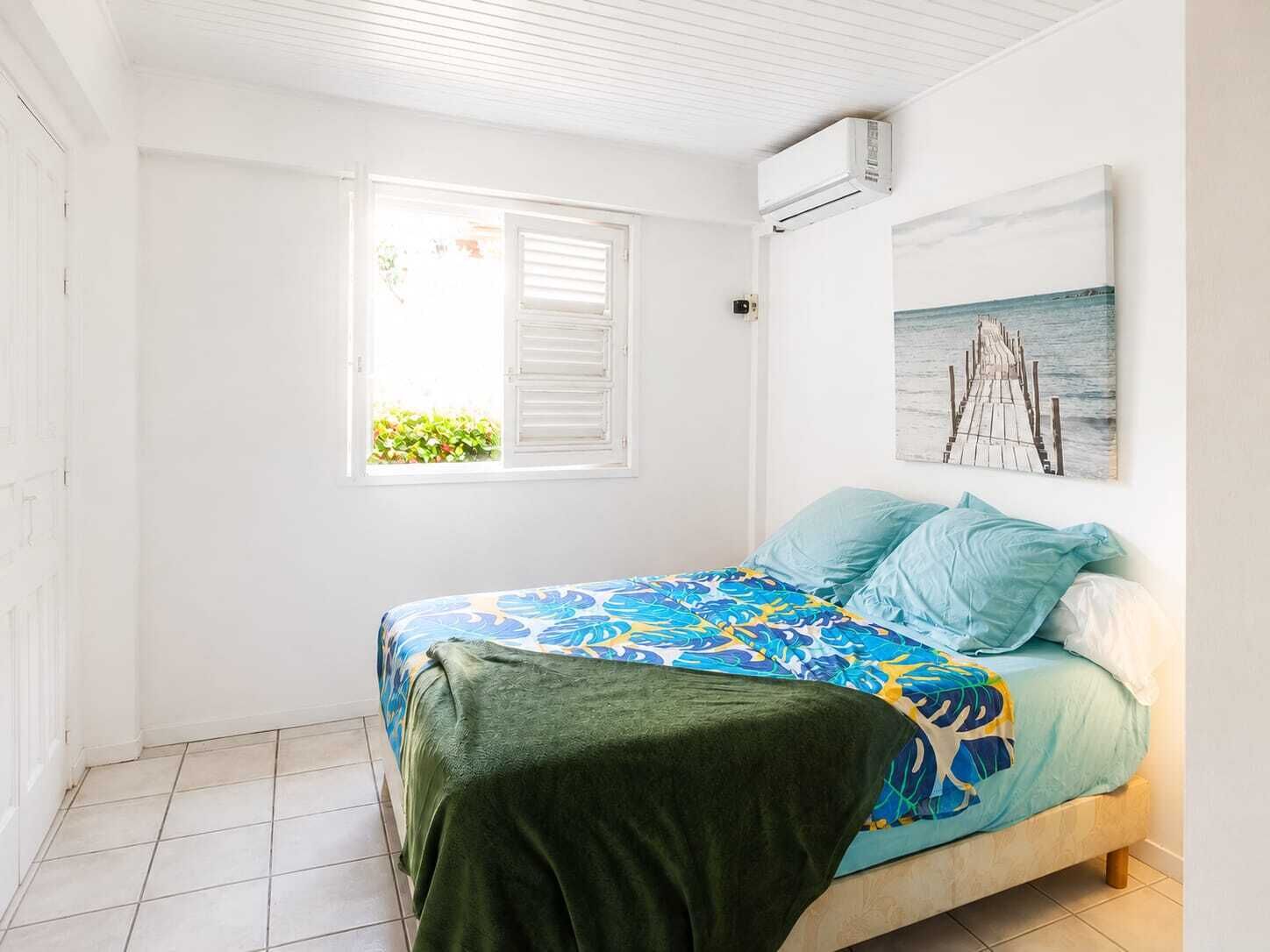 A bedroom with a bed, a window, an air conditioning unit, and a wall-mounted picture.