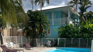A swimming pool with a stone-tiled deck, surrounded by lounge chairs and a white fence. - LILI Apartment with swimming pool, 400m from the beach. (Les Trois-Îlets)