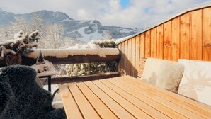 Eine Holzterrasse mit einer Bank und Kissen, mit Blick auf eine verschneite Berglandschaft.