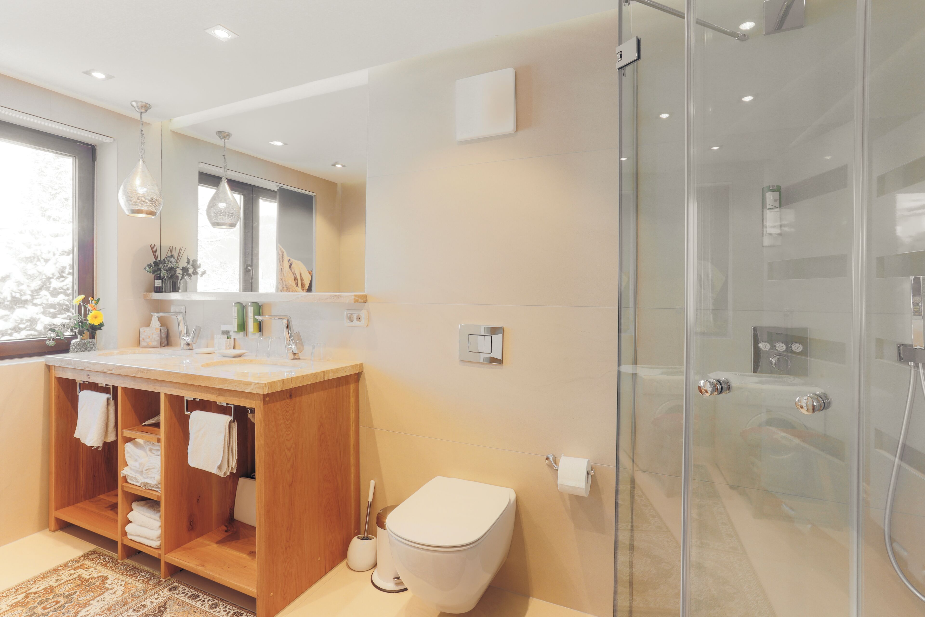 A modern bathroom with a wooden vanity, a glass shower enclosure, and a large mirror above the sink.