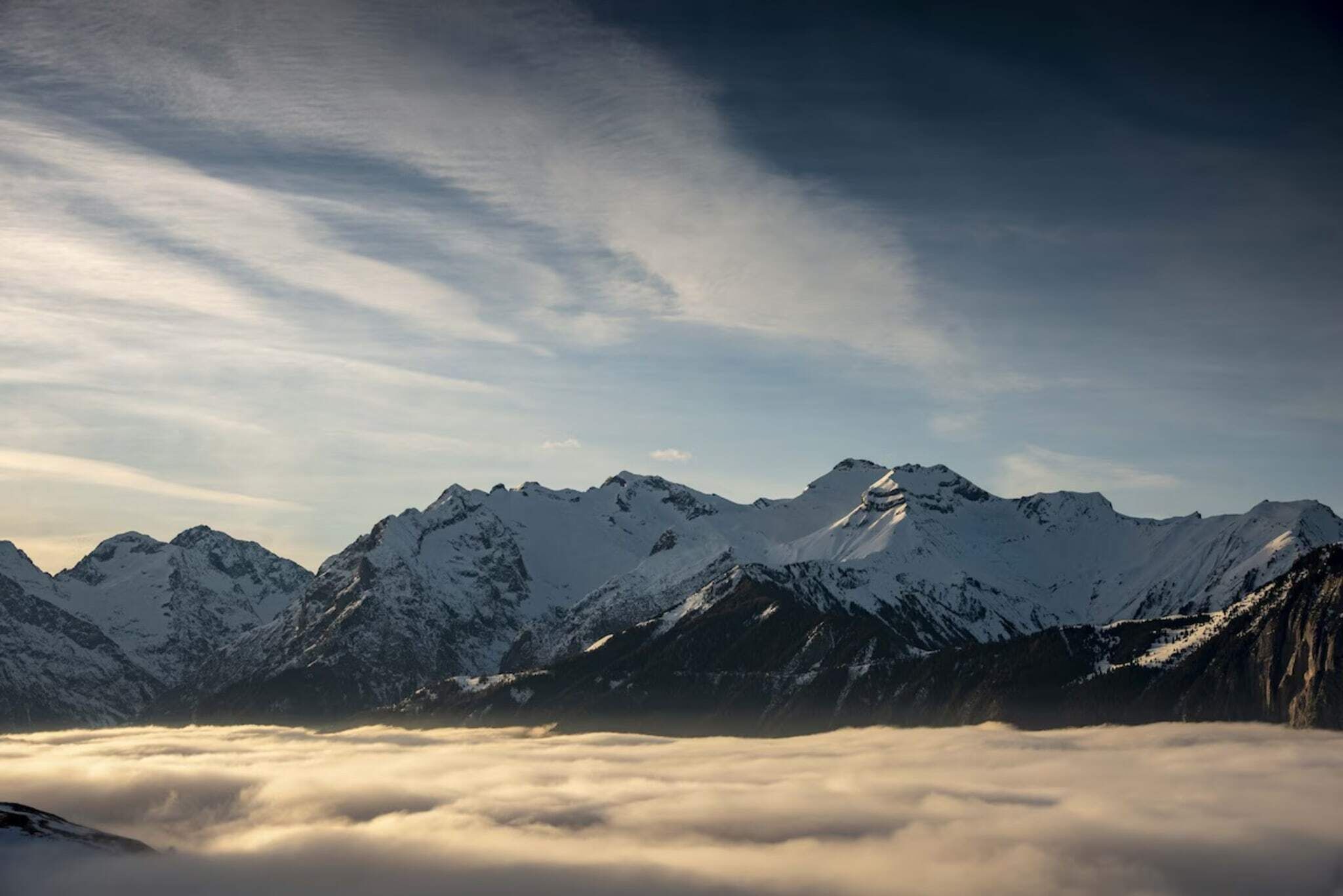 Ein Gebirge mit schneebedeckten Gipfeln und einer Wolkenschicht darunter.