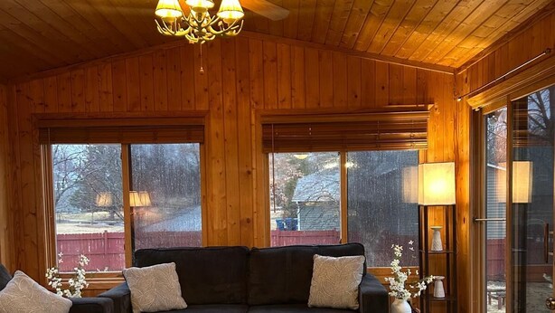 A cozy cabin interior with a wooden ceiling, a black sofa set, a fluffy white ottoman, and a ceiling fan. - 4-bedroom home in Eagen,family friendly, centrally located with fenced backyard (Eagan)