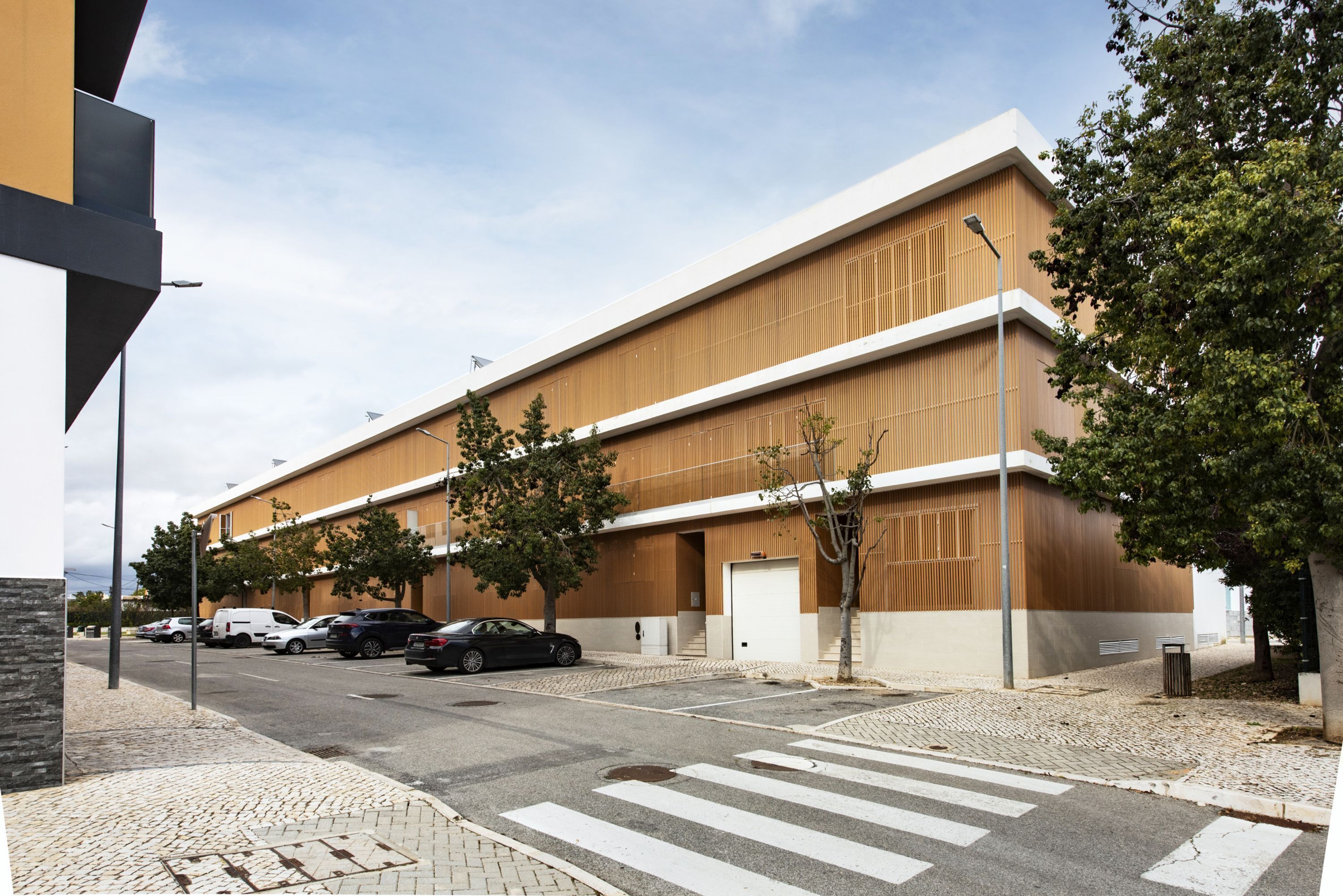 A modern building with a flat roof, large windows, and a parking lot with several cars.