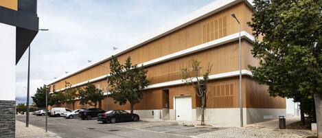 A modern building with a flat roof, large windows, and a parking lot with several cars.