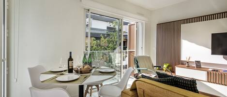 A modern living room with a dining area, large windows, a flat-screen TV, and a sofa.