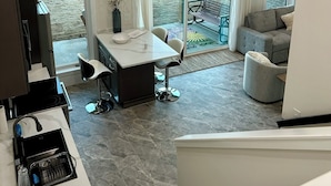 A modern kitchen with a dining area, a grey sofa, and a large sliding glass door leading to an outdoor patio. - Newly Built, Modern Home Sleeps 10 on Houston Lake in beautiful Perry, GA! (Perry)