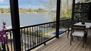 A wooden deck with a table and chairs, overlooking a lake with a view of trees and a distant house. - Newly Built, Modern Home Sleeps 10 on Houston Lake in beautiful Perry, GA! (Perry)
