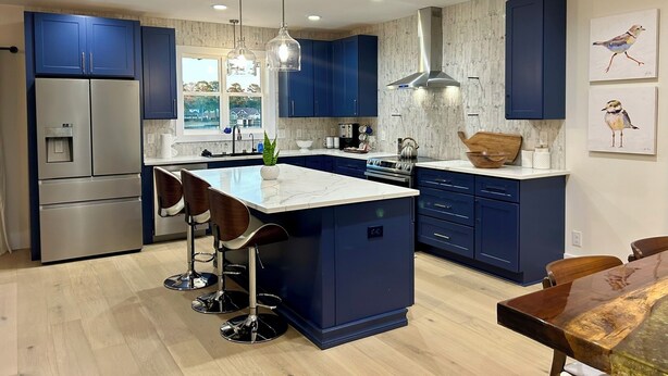 A modern kitchen with blue cabinets, a central island with bar stools, stainless steel appliances, pendant lighting, and artwork on the wall. - Newly Built, Modern Home Sleeps 10 on Houston Lake in beautiful Perry, GA! (Perry)