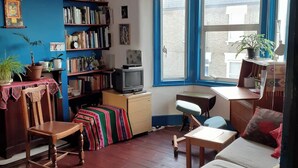 Ein gemütliches Wohnzimmer mit Holzboden, einer Couch, einem Sessel, einem kleinen Tisch und einem Bücherregal.