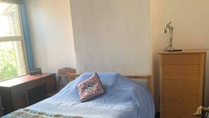 Ein Schlafzimmer mit einem Bett, einer Holzkommode, einem Schreibtisch und einem Fenster.