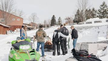 Un groupe de personnes s’est rassemblé autour d’un motoneige et d’un foyer dans un décor enneigé en plein air.