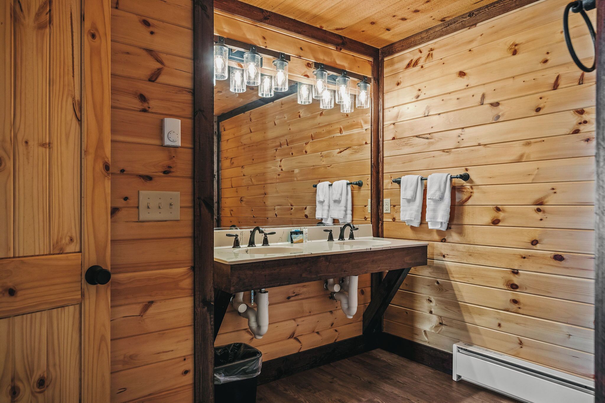 Ein Badezimmer mit Holzwänden, einem Doppelwaschbecken, einem Spiegel und Pendelleuchten.