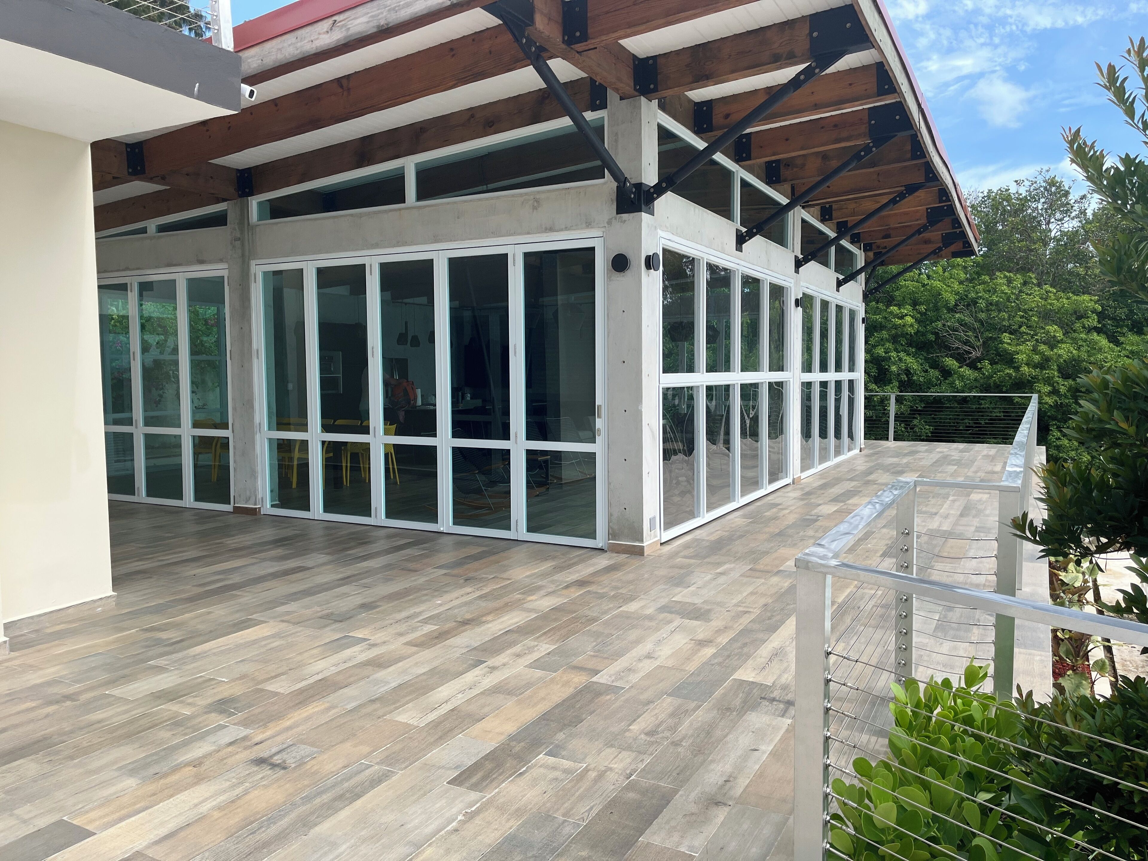 Un edificio moderno con amplios ventanales, una terraza de madera y una barandilla de metal.