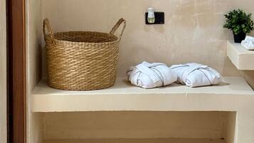 Een badkamer met een gevlochten mand, twee opgerolde handdoeken, een klein flesje en een potplant.