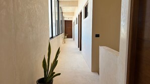 A corridor with a potted plant, beige walls, and a wooden door at the end. - Ananda Hotel Boutique (Isla Holbox)