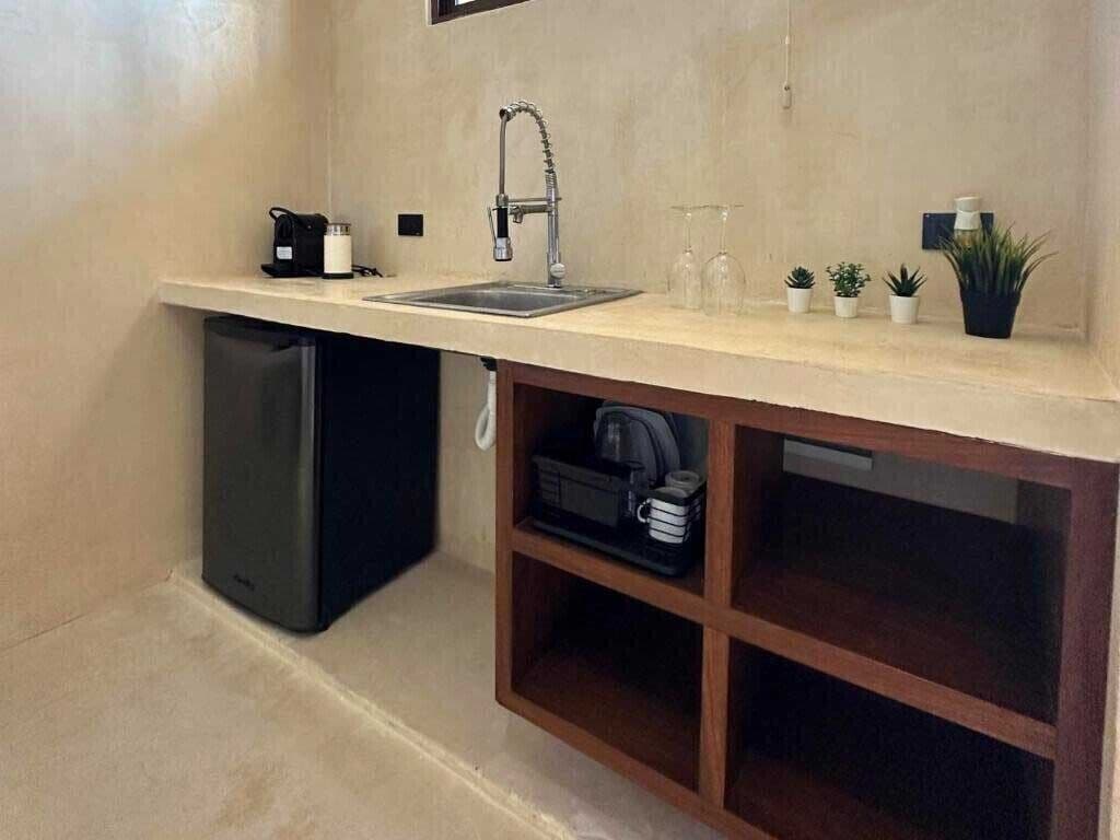 A compact kitchenette with a sink, a coffee maker, a small refrigerator, and a wooden shelf with storage.