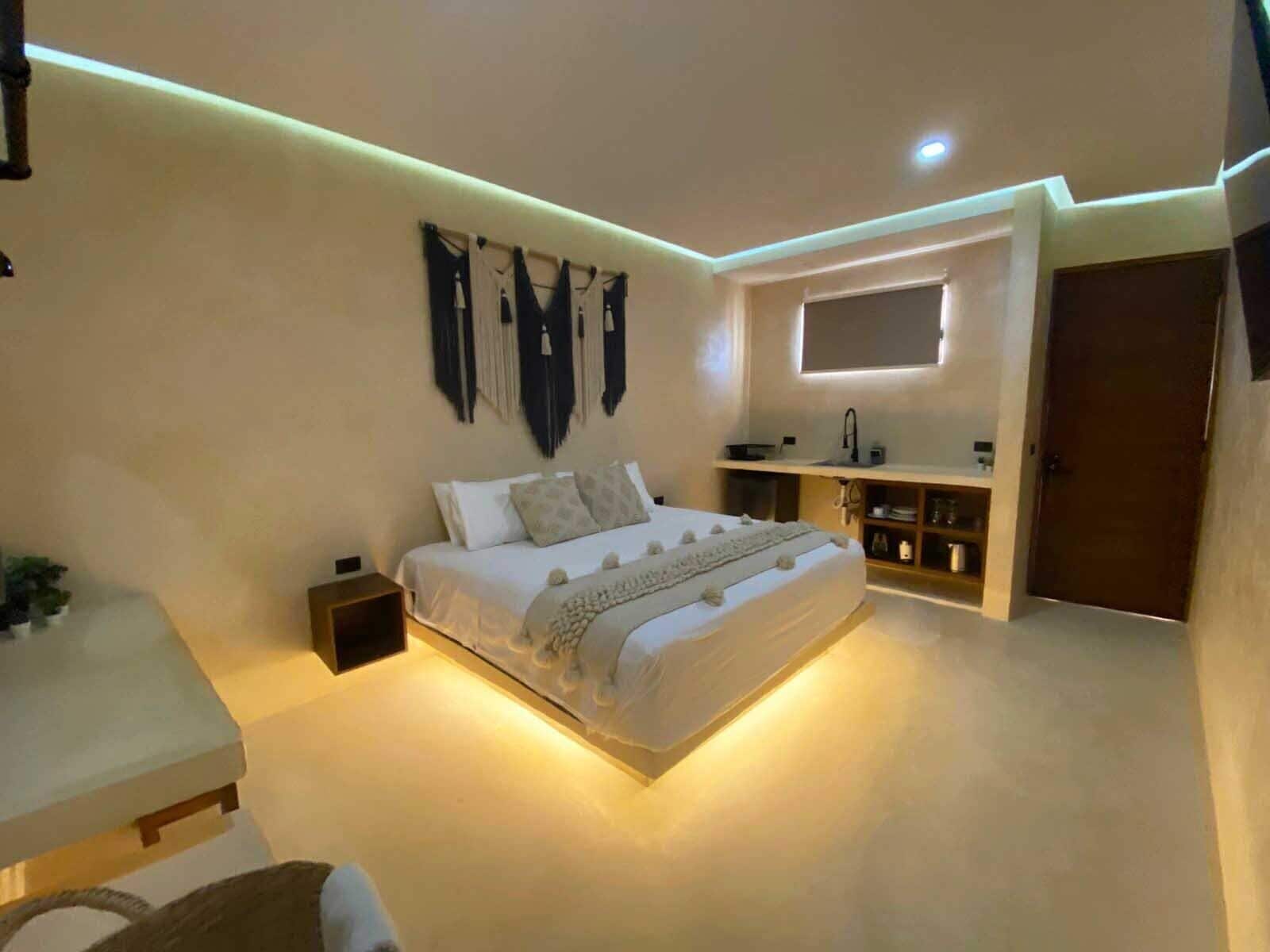 A modern bedroom with a bed, bedside table, wall-mounted artwork, and a built-in shelf with a mirror.