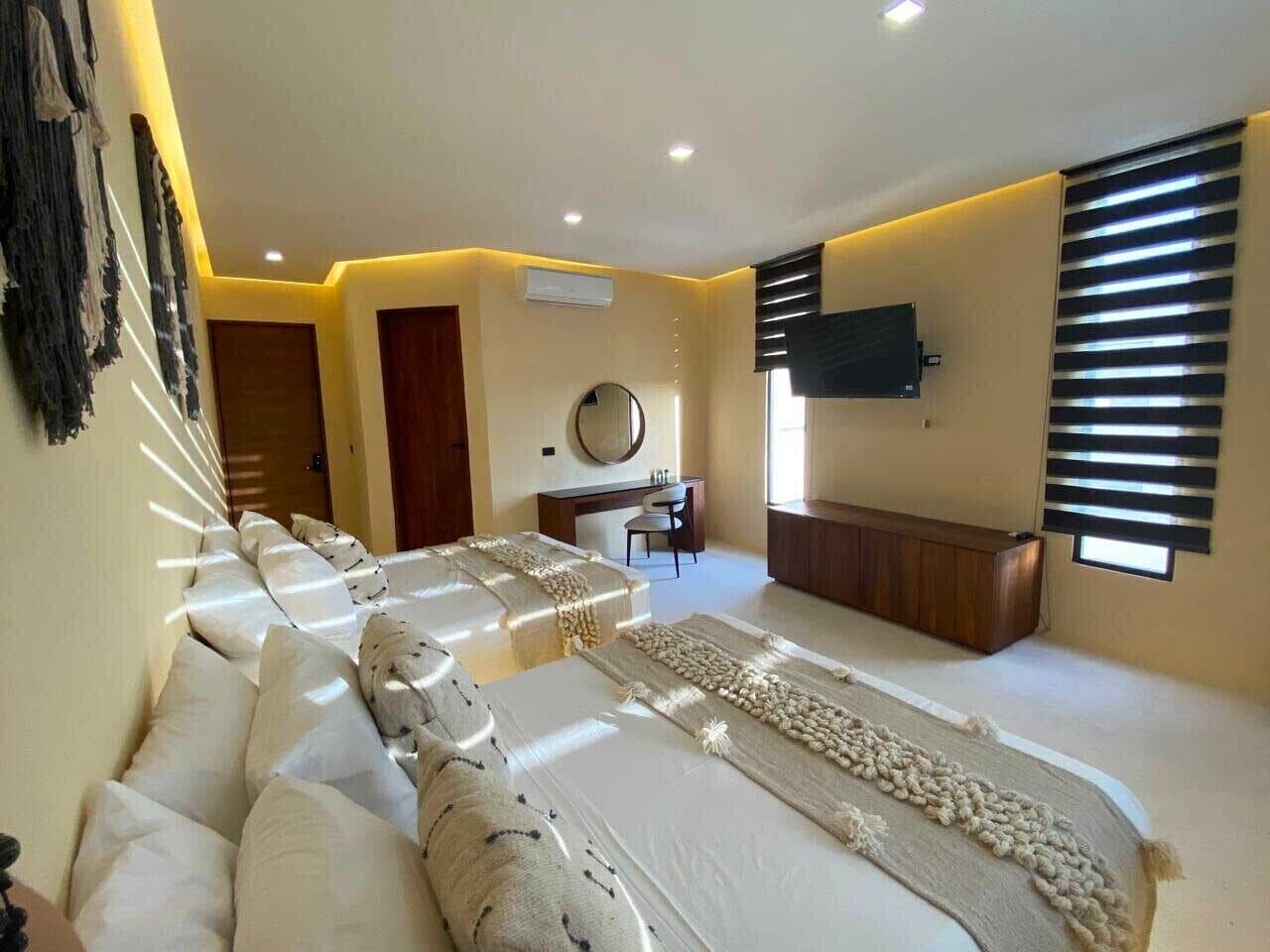 Une chambre d’hôtel avec un grand lit, un bureau, une chaise, une télévision et une fenêtre avec des stores.