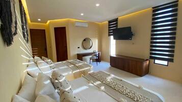 A hotel room with a long bed, a desk, a chair, a TV, and a window with blinds.